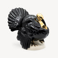 Three-quarter view of a glossy black Goebel porcelain turkey sculpture with a gold head and claws on a white base